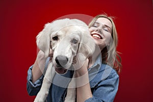 Young beautiful girl holding a golden retriever puppy in her arms on a red background, close-up of the dogs face smiling, funny