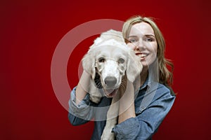 Young beautiful girl holding a golden retriever puppy in her arms on a red background, close-up of the dogs face smiling, funny