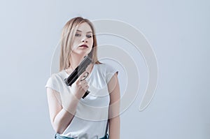Young beautiful girl holding a gun in her hands. Pistol raised up to face