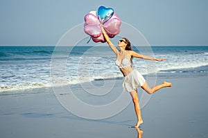 Young and beautiful girl holding helium balloons air, running and jumping for joy at the sea. holiday and vacation
