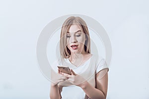 Young beautiful girl holding a mobile phone in her hands. Looks surprised at the screen