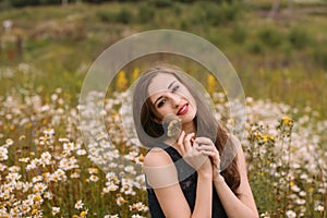 Young beautiful girl holds flowers in hands in chamomile field