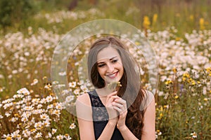 Young beautiful girl holds flowers in hands in chamomile field