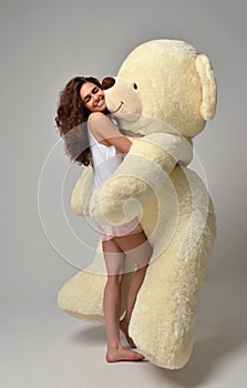 Young beautiful girl hugging big teddy bear soft toy happy smiling