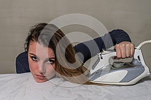 Young beautiful girl ironing her hair on an ironing board