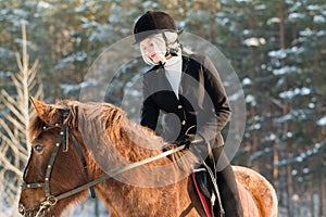 Young beautiful girl jockey riding a horse in winter forest