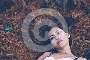 Young beautiful girl laying on the forest floor, with hair tangled in small branches that felled from pine trees, fashion concept