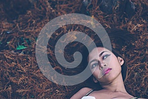 Young beautiful girl laying on the forest floor, with hair tangled in small branches that felled from pine trees, fashion concept