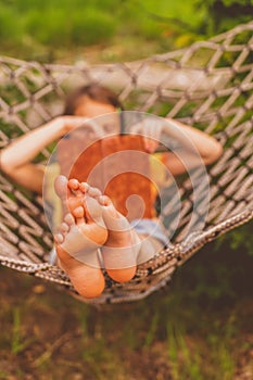 A young beautiful girl lies in a hammock and reads a book. Rest, summer vacation, leisure time concept. Selective focus on feets.
