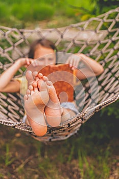 A young beautiful girl lies in a hammock and reads a book. Rest, summer vacation, leisure time concept. Selective focus on feets