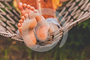 A young beautiful girl lies in a hammock and reads a book.  Selective focus on feets. Horizontal image