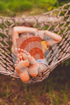A young beautiful girl lies in a hammock. Rest, summer vacation, leisure time concept. Selective focus on feets. Vertical image