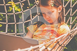 A young beautiful girl lies in a hammock and working remotely with laptop