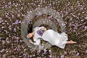 A young beautiful girl lies with her eyes closed in a blooming field of Provence. Romantic atmosphere