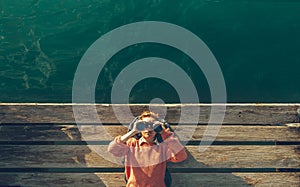 Young Beautiful Girl Lies On A Pier Near The Sea And Looks Through Binoculars On The Sky. Travel Search Journey Concept photo