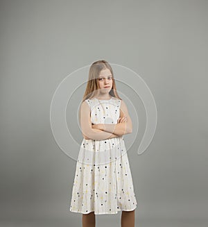 a young beautiful girl in a light dress stands with a sad face on a gray isolated background.