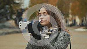 Young beautiful girl lipstick hygienic lipstick on a city street. Autumn. Cold.