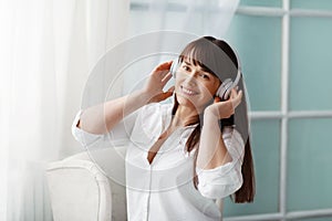 Young beautiful girl listening to music with headphones. The girl is enjoying the music sitting by the window. Rest, relaxation
