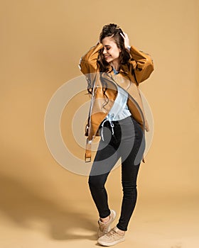 Young beautiful girl with long curly hair in a brown leather jacket holds her head with her hands on an orange studio background