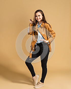 Young beautiful girl with long curly hair in a brown leather jacket posing on a pastel orange studio background