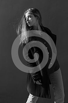 Young beautiful girl with long hair in black coat on sunny day turns around against the wall. Street style portrait