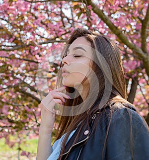 Young beautiful girl with long hair enjoys the beauty of spring nature near the blossoming sakura tree