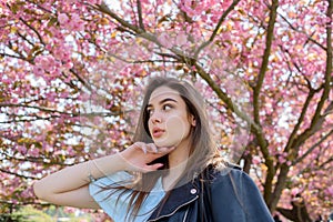 Young beautiful girl with long hair enjoys the beauty of spring nature near the blossoming sakura tree