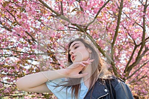 Young beautiful girl with long hair enjoys the beauty of spring nature near the blossoming sakura tree
