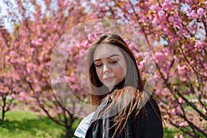 Young beautiful girl with long hair enjoys the beauty of spring nature near the blossoming sakura tree