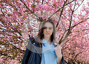 Young beautiful girl with long hair enjoys the beauty of spring nature near the blossoming sakura tree