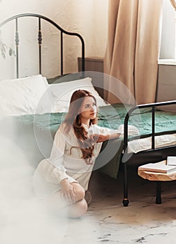 Young beautiful girl with long hair in a white shirt resting in the bedroom. The concept of home coziness and comfort