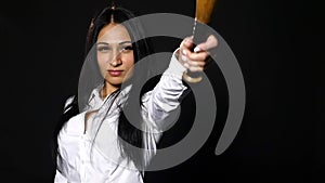 Young beautiful girl looking at camera brutally, holding bat over black background