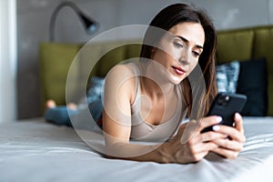 Young beautiful girl looking at a mobile phone while lying in bed