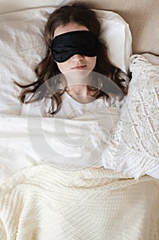 Young beautiful girl lying in comfortable bed wearing sleep mask in the morning at cozy room. Concept of rest at home