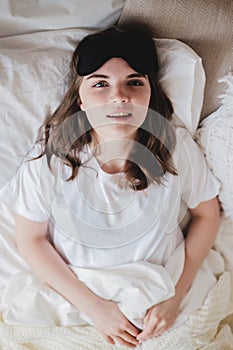 Young beautiful girl lying in comfortable bed wearing sleep mask in the morning at cozy room. Concept of rest at home