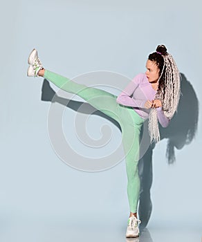Young beautiful girl with modern hairstyle in sportswear standing and making kick by leg