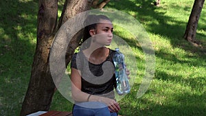 Young beautiful girl opens a plastic bottle with water and drinks water from her.