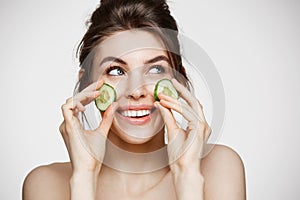 Young beautiful girl with perfect clean skin smiling holding cucumber slices over white background. Beauty cosmetology