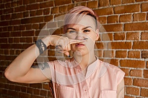 Young beautiful girl pinches fingers with a stink on brick wall background