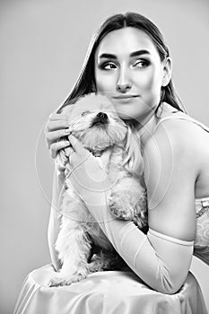 A young beautiful girl in a pink dress with a white small dog on a pink background