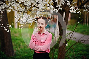 Young beautiful girl in a pink shirt standing under blossoming apple tree and enjoying a sunny day.