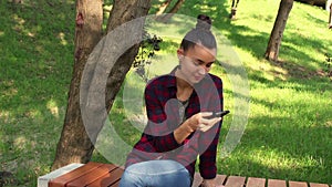 Young beautiful girl in a plaid shirt smiling and browsing the tape of social networks in her smartphone.