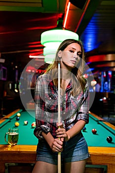 Young beautiful girl is playing billiards. Pleasant pastime, rest, entertainment.