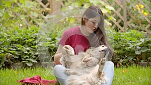 Young, beautiful girl playing with dog in garden.The girl plays with the dog on a lawn. The girl plays about with the