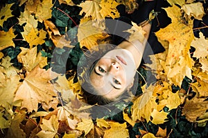 Young beautiful girl portrait lying in autumn leaves.