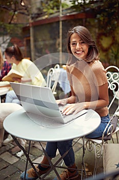 A young beautiful girl is posing for a photo while sitting in the bar and chatting on the laptop. Leisure, bar, outdoor