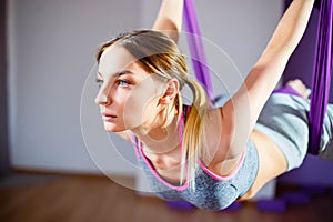 Young beautiful girl practicing aerial yoga in gym