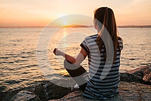 Young beautiful girl practicing yoga and meditation on the rocks next to the sea at sunset. Sport. Yoga. Meditation