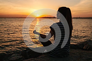 Young beautiful girl practicing yoga and meditation on the rocks next to the sea at sunset. Sport. Yoga. Meditation