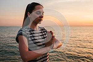 Young beautiful girl practicing yoga and meditation on the rocks next to the sea at sunset. Sport. Yoga. Meditation